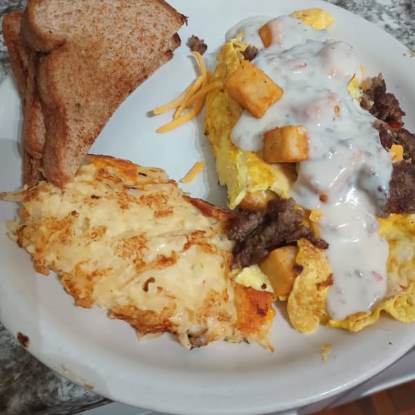 Southern breakfast plate with hash browns, scrambled eggs, sausage gravy, and toast.