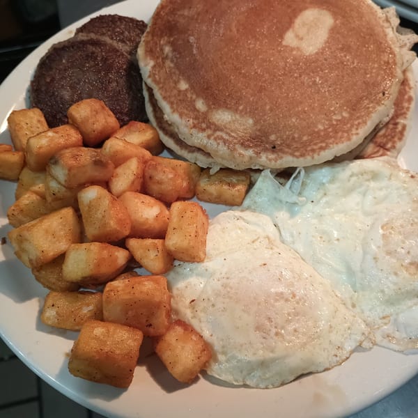 A Southern Taste Cafe breakfast plate with pancakes, sausage patties, crispy hash browns, and fried eggs.