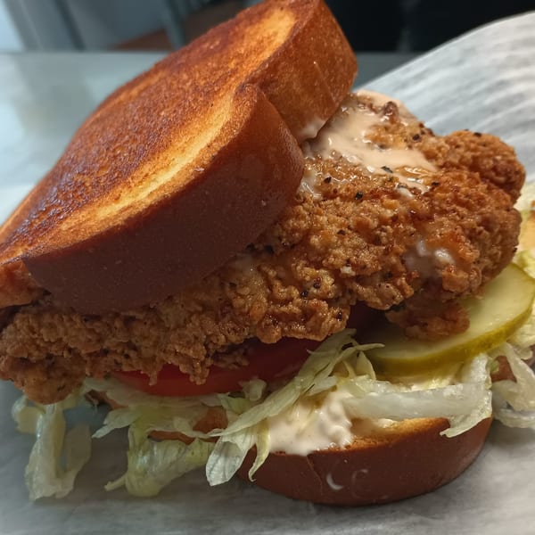 Southern fried chicken sandwich with sauce, pickles, lettuce, and tomato on toasted bread.