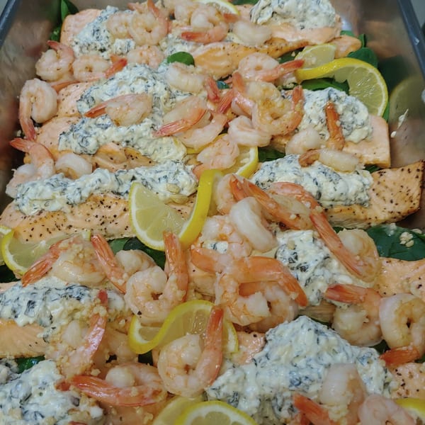 Baked salmon fillets topped with creamy spinach, shrimp, and lemon slices in a metal pan.