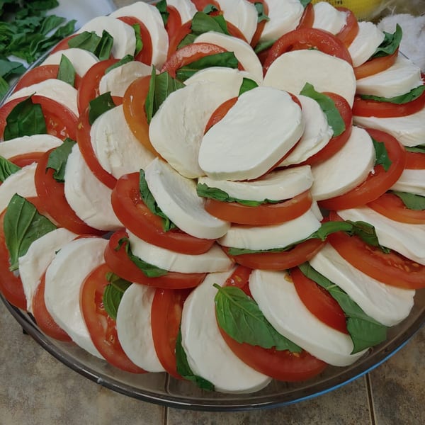 A platter of Caprese salad with sliced tomatoes, fresh mozzarella, and basil leaves.