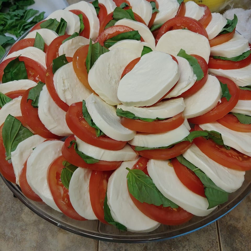 A platter of Caprese salad with sliced tomatoes, fresh mozzarella, and basil leaves.