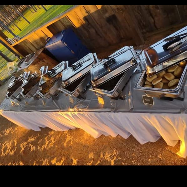 A buffet line of Southern Taste Cafe's southern dishes, including rolls, in chafing dishes outdoors.