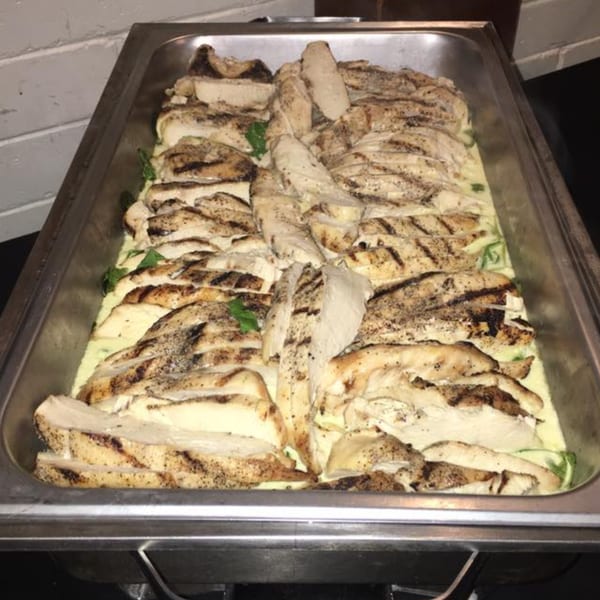 Grilled chicken slices with seasoning, served in a creamy sauce in a metal chafing dish.